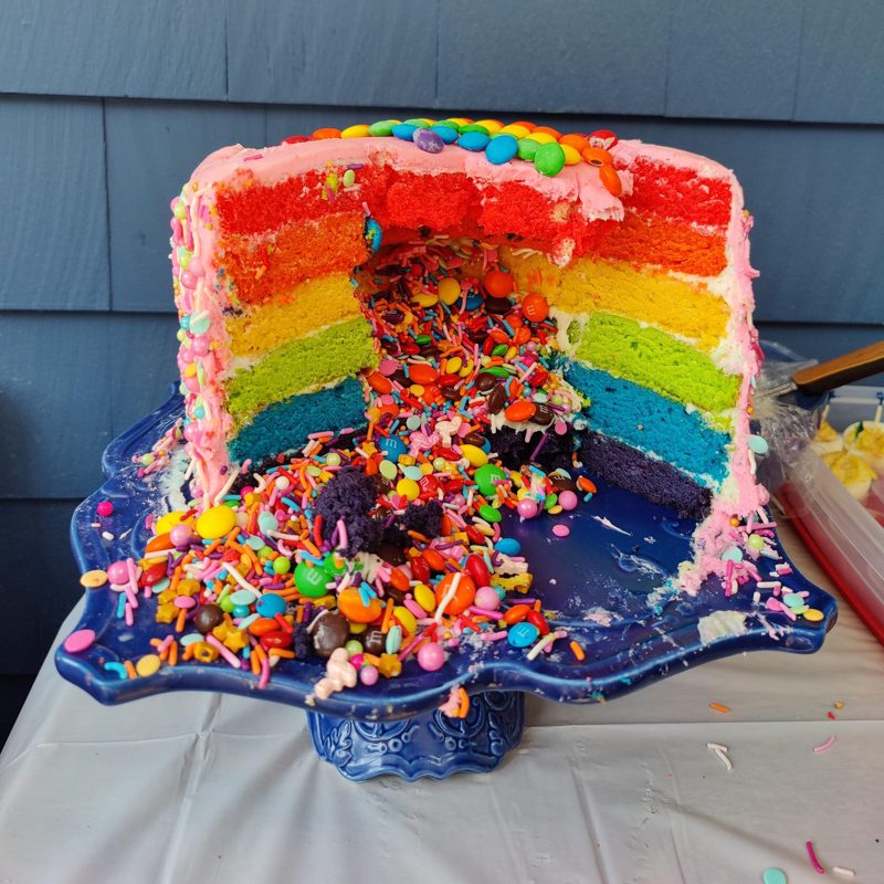 Rainbow layer cake cut open with candy spilling out