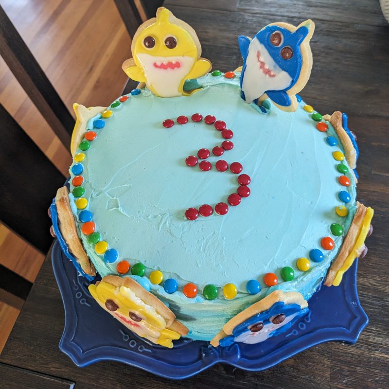 Blue cake with a candy number 3 and shark cookies